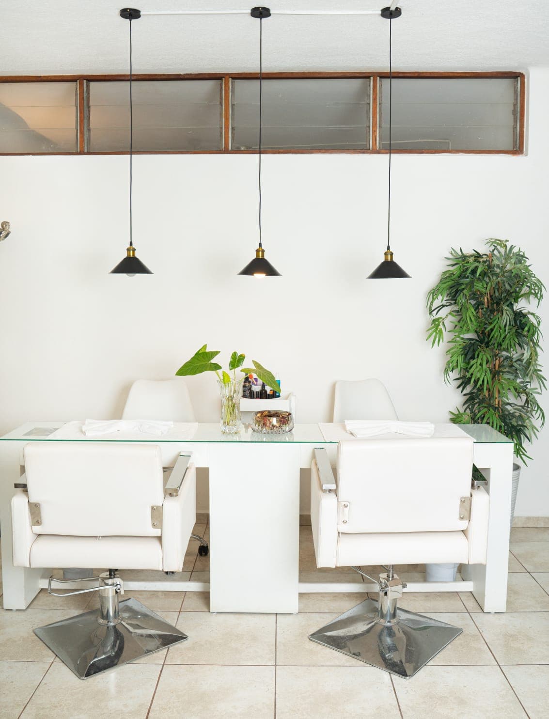 Manicure station with a glass table, white chairs and pendant lights