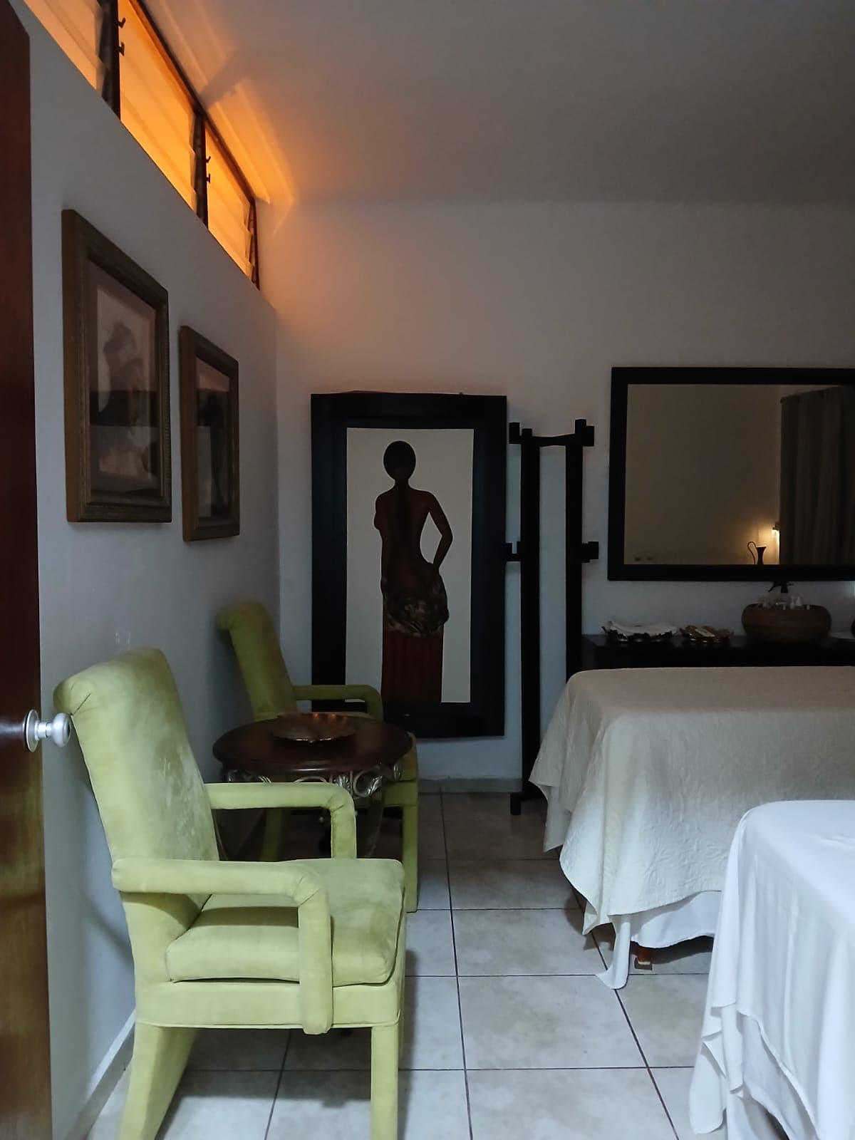 Massage treatment room with a dressed table and soft green chairs